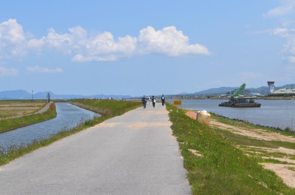 十四間川堤防を歩く人たち 青い空と水、堤防の緑、白い雲に気持ちよさそう
